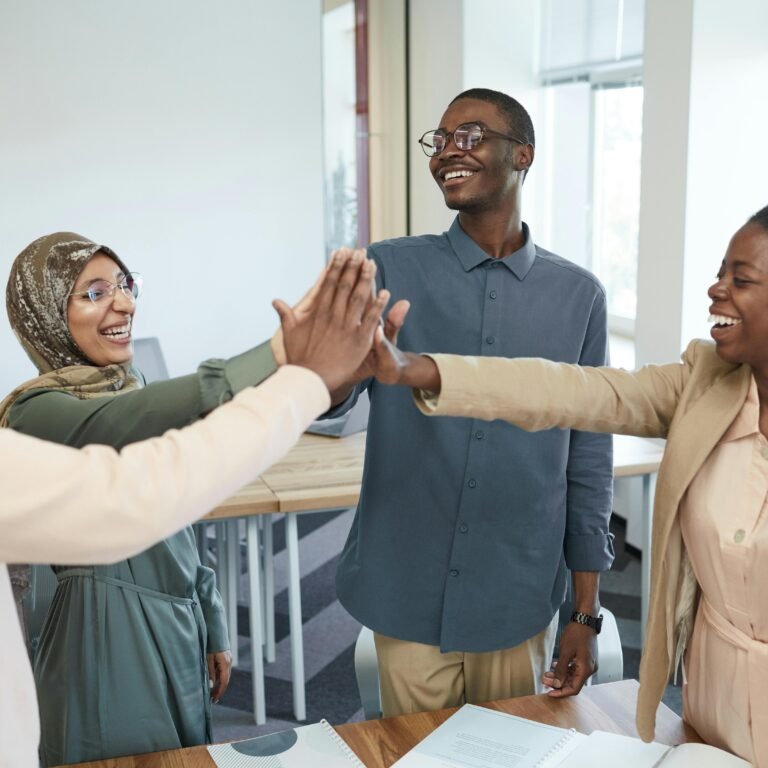 A joyful group of diverse colleagues high-fiving each other in an office, symbolizing teamwork and collaboration.